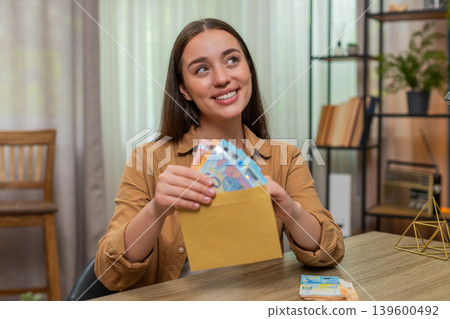 Woman counting euro cash money placing bills into envelope pleased with careful budget planning Woman counting euro cash money placing bills into envelope pleased with careful budget planning 139600492