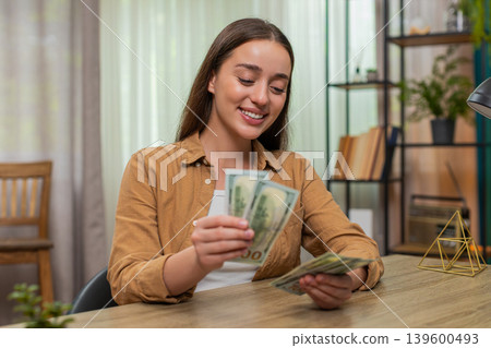 Young woman counting money dollars cash satisfied with salary earnings celebrating financial success Young woman counting money dollars cash satisfied with salary earnings celebrating financial success 139600493