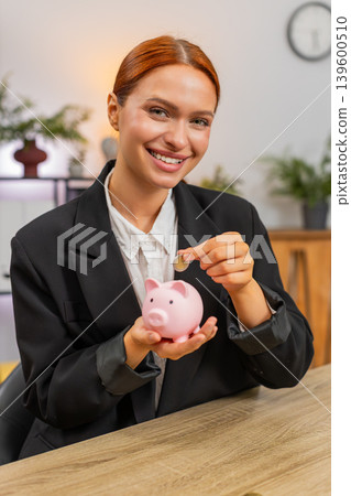 Young businesswoman drops coins into piggy bank planning future savings wealth growth security goal Young businesswoman drops coins into piggy bank planning future savings wealth growth security goal 139600510