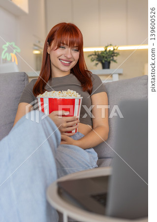 Young woman with bowl of popcorn laughs at movie trailer on laptop smiles happy reaction fun watch Young woman with bowl of popcorn laughs at movie trailer on laptop smiles happy reaction fun watch 139600526