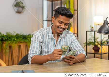 Indian man counts dollar cash salary bonus plans invest smiles feels proud profit wealth success joy Indian man counts dollar cash salary bonus plans invest smiles feels proud profit wealth success joy 139600527
