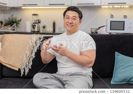 Asian man holds cup of herbal tea warms hands smiles breathes aroma enjoys pause mindful calm break 139600532