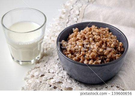 Cooked buckwheat porridge in a ceramic bowl and a glass of fresh milk on a linen tablecloth Cooked buckwheat porridge in a ceramic bowl and a glass of fresh milk on a linen tablecloth 139600656