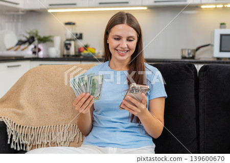 Young woman counts dollars money cash with smartphone checks exchange rate plans purchase invests Young woman counts dollars money cash with smartphone checks exchange rate plans purchase invests 139600670