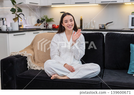 Young woman waves hello smiles greeting camera hand gesture cheerful welcome sign positive mood warm Young woman waves hello smiles greeting camera hand gesture cheerful welcome sign positive mood warm 139600671