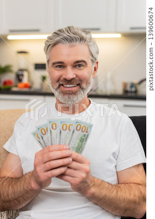 Middle-aged man counts money cash dollars smiles at plans purchase salary bonus savings investment Middle-aged man counts money cash dollars smiles at plans purchase salary bonus savings investment 139600674