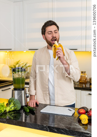Middle-aged man peeling banana in home kitchen enjoying healthy snack for diet and fitness lifestyle Middle-aged man peeling banana in home kitchen enjoying healthy snack for diet and fitness lifestyle 139600706