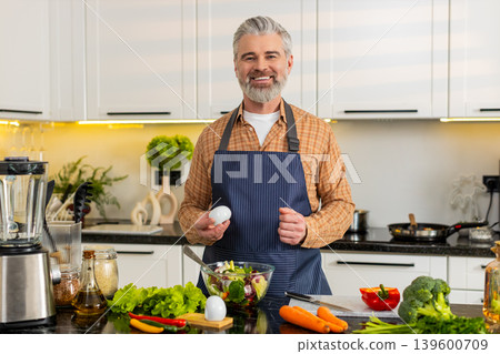 Middle-aged man seasoning fresh salad in kitchen for healthy diet meal prep wellness goals at home 139600709