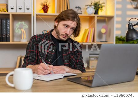 Young man on home table studying with laptop video lesson and writing notes during online learning 139600743