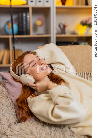 Young woman on home sofa relaxing with headphones and closed eyes while listening to peaceful music Young woman on home sofa relaxing with headphones and closed eyes while listening to peaceful music 139600745