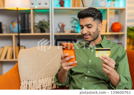 Indian man on home sofa shopping online with smartphone and bank card smiling after successful order Indian man on home sofa shopping online with smartphone and bank card smiling after successful order 139600761