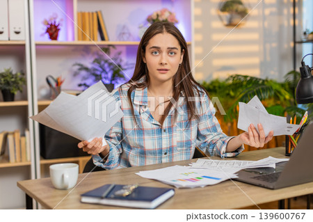 Young woman on home table upset with receipts and documents throwing papers in frustration at laptop Young woman on home table upset with receipts and documents throwing papers in frustration at laptop 139600767