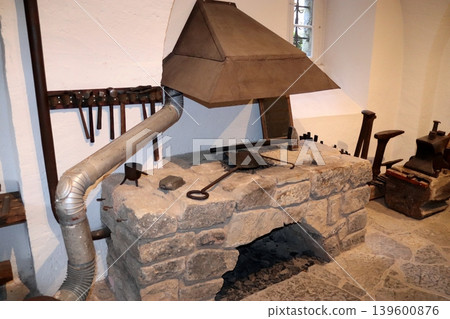 An antique stone forge with a hood in a workshop. An antique stone forge with a hood in a workshop. 139600876