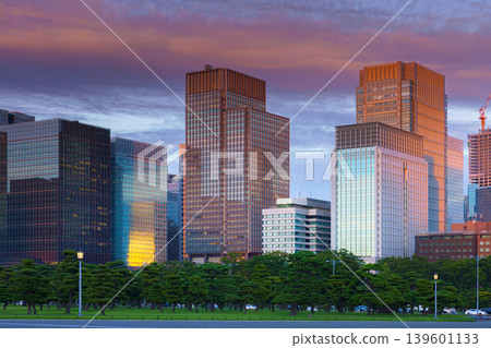 Tokyo, Japan - Oct 1 2024, panoramic view of the Chiyoda district's skyscrapers, with a parking lot with people walking in the foreground, and colorful clouds at sunset.Tokyo, Japan Tokyo, Japan - Oct 1 2024, panoramic view of the Chiyoda district's skyscrapers, with a parking lot with people walking in the foreground, and colorful clouds at sunset.Tokyo, Japan 139601133