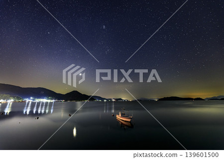 Summer starry sky over the Seto Inland Sea: Orion rising in the sky above the fishing port. Summer starry sky over the Seto Inland Sea: Orion rising in the sky above the fishing port. 139601500