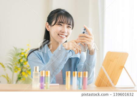 一位年輕女子早上正在用智慧型手機梳妝打扮。 一位年輕女子早上正在用智慧型手機梳妝打扮。 139601632