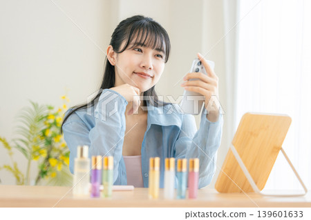 一位年輕女子早上正在用智慧型手機梳妝打扮。 一位年輕女子早上正在用智慧型手機梳妝打扮。 139601633