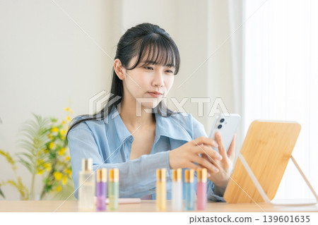 一位年輕女子早上正在用智慧型手機梳妝打扮。 一位年輕女子早上正在用智慧型手機梳妝打扮。 139601635