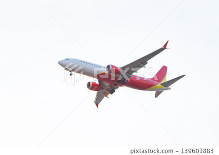 Modern commercial jet with red and yellow accents flying at low altitude with deployed landing gear against a bright evening sky. Modern commercial jet with red and yellow accents flying at low altitude with deployed landing gear against a bright evening sky. 139601883