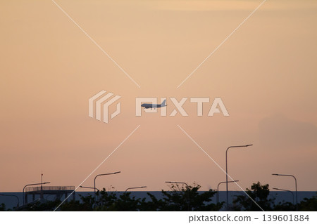 Distant commercial aircraft approaching for landing over urban skyline with glowing evening sky and dramatic sunset atmosphere. Distant commercial aircraft approaching for landing over urban skyline with glowing evening sky and dramatic sunset atmosphere. 139601884