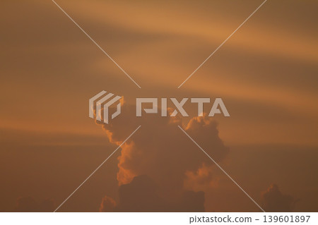 Dramatic towering cloud illuminated by warm sunset light against a deep orange sky, creating a moody atmospheric nature background with soft glowing tones. Dramatic towering cloud illuminated by warm sunset light against a deep orange sky, creating a moody atmospheric nature background with soft glowing tones. 139601897