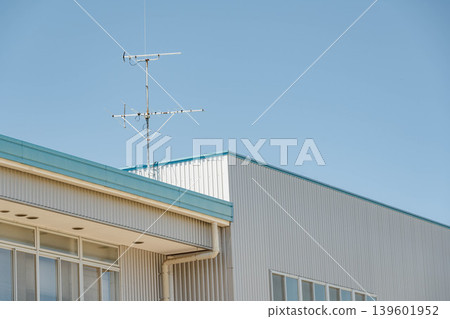 A building with a blue sky and white exterior walls, and a television antenna on the roof. A building with a blue sky and white exterior walls, and a television antenna on the roof. 139601952