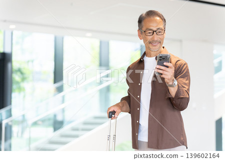 Senior male traveler staying at a hotel, booking via smartphone. Senior male traveler staying at a hotel, booking via smartphone. 139602164