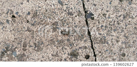 Close up of an asphalt concrete surface with natural cracks and small stone details scattered throughout the surface. Close up of an asphalt concrete surface with natural cracks and small stone details scattered throughout the surface. 139602627