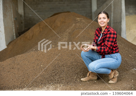 Joyful woman farmer at heap of rapeseed oil cake, animal food Joyful woman farmer at heap of rapeseed oil cake, animal food 139604064
