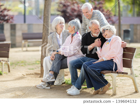 Group of elderly men and women chatting on bench in courtyard Group of elderly men and women chatting on bench in courtyard 139604132