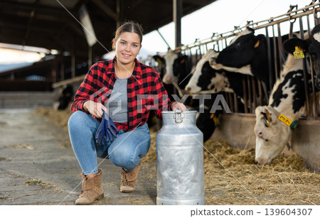 Positive young woman farmer squatting at milk can Positive young woman farmer squatting at milk can 139604307