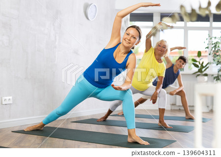Mom, grandmother and teen grandson performing lateral elongated angle pose Utthita Parshvakonasana Mom, grandmother and teen grandson performing lateral elongated angle pose Utthita Parshvakonasana 139604311