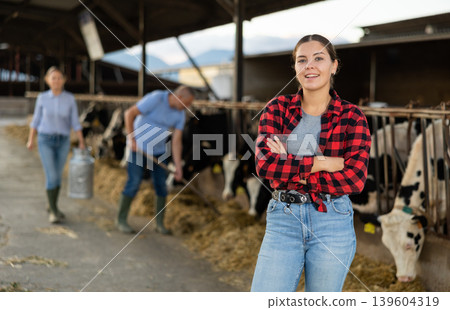 Successful girl farmer standing in open cowshed at dairy cow farm Successful girl farmer standing in open cowshed at dairy cow farm 139604319