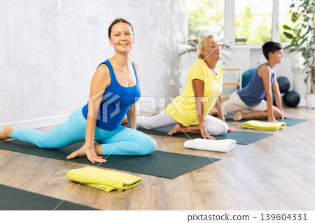 Mother, grandmother and teen son do exercise dove pose, Eka Pada Rajakapotasana. Mother, grandmother and teen son do exercise dove pose, Eka Pada Rajakapotasana. 139604331