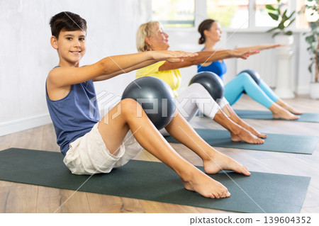 Family grandmother, mother and grandson perform fitness exercise sitting on floor with softball Family grandmother, mother and grandson perform fitness exercise sitting on floor with softball 139604352