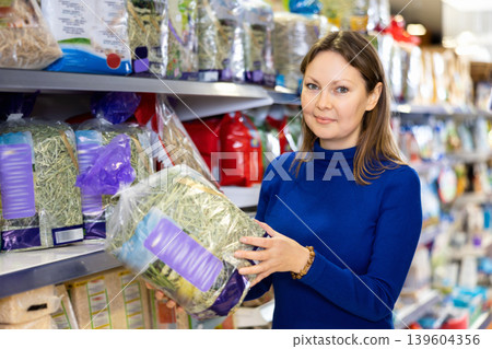 Young woman choosing dry straw for bedding for rabbit cage Young woman choosing dry straw for bedding for rabbit cage 139604356