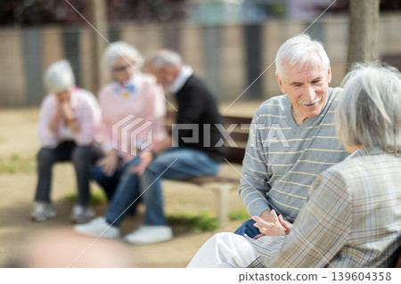 Elderly couple flirting while sitting on bench in courtyard 139604358