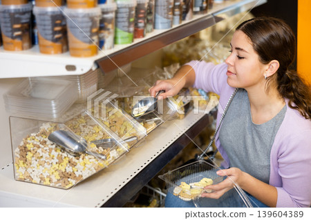 Young female customer picking out dry pet treats in pet store Young female customer picking out dry pet treats in pet store 139604389