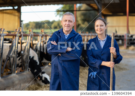 Aged farmer posing with adult daughter in cowshed at family farm Aged farmer posing with adult daughter in cowshed at family farm 139604394