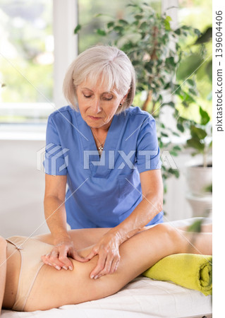 Professional mature masseuse doing anti-cellulite thigh massage to young woman Professional mature masseuse doing anti-cellulite thigh massage to young woman 139604406