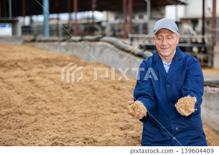 Middle-aged man farmer checking beer oilcake in fodder storage Middle-aged man farmer checking beer oilcake in fodder storage 139604409