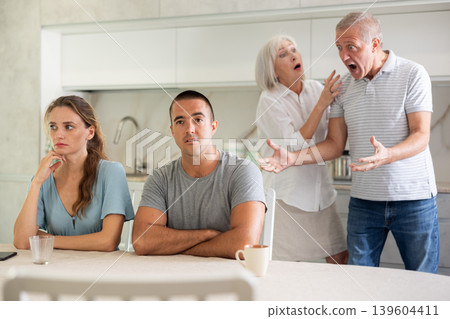 Elderly parents make claims to young couple in kitchen Elderly parents make claims to young couple in kitchen 139604411