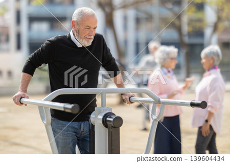 Group of elderly people exercising using equipment in courtyard Group of elderly people exercising using equipment in courtyard 139604434