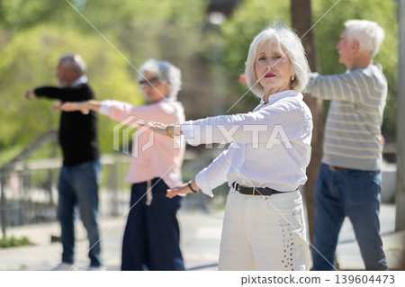 Group of elderly people perform arm swinging exercise physical activity outdoors. 139604473