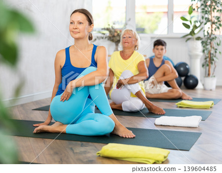 Middle-aged woman practicing lord of the fishes pose of yoga in light fitness room Middle-aged woman practicing lord of the fishes pose of yoga in light fitness room 139604485