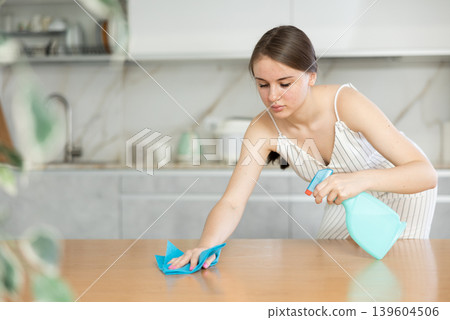Smiling housewife with rag and detergent spray polish cleans dining table from grease and dirt 139604506