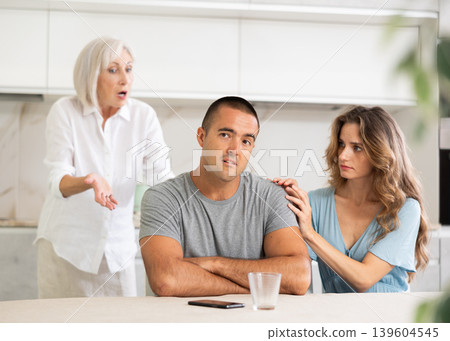 Elderly woman quarrels with couple in kitchen Elderly woman quarrels with couple in kitchen 139604545