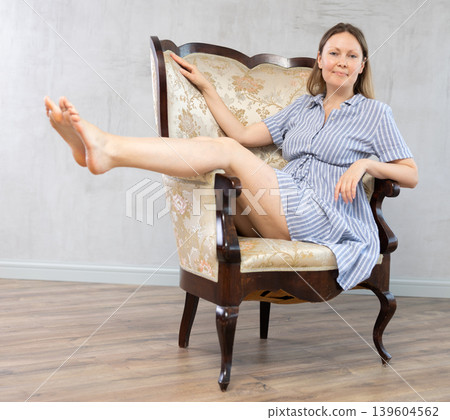 Girl settled down in vintage armchair with legs raised on armrest , put feet on handle of furniture Girl settled down in vintage armchair with legs raised on armrest , put feet on handle of furniture 139604562