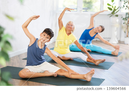 Preteen boy practicing revolved head to knee pose of yoga in light fitness room 139604566