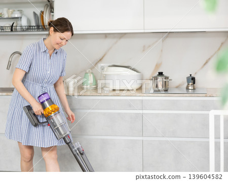 Housewife using vacuum cleaner removes dust in room Housewife using vacuum cleaner removes dust in room 139604582